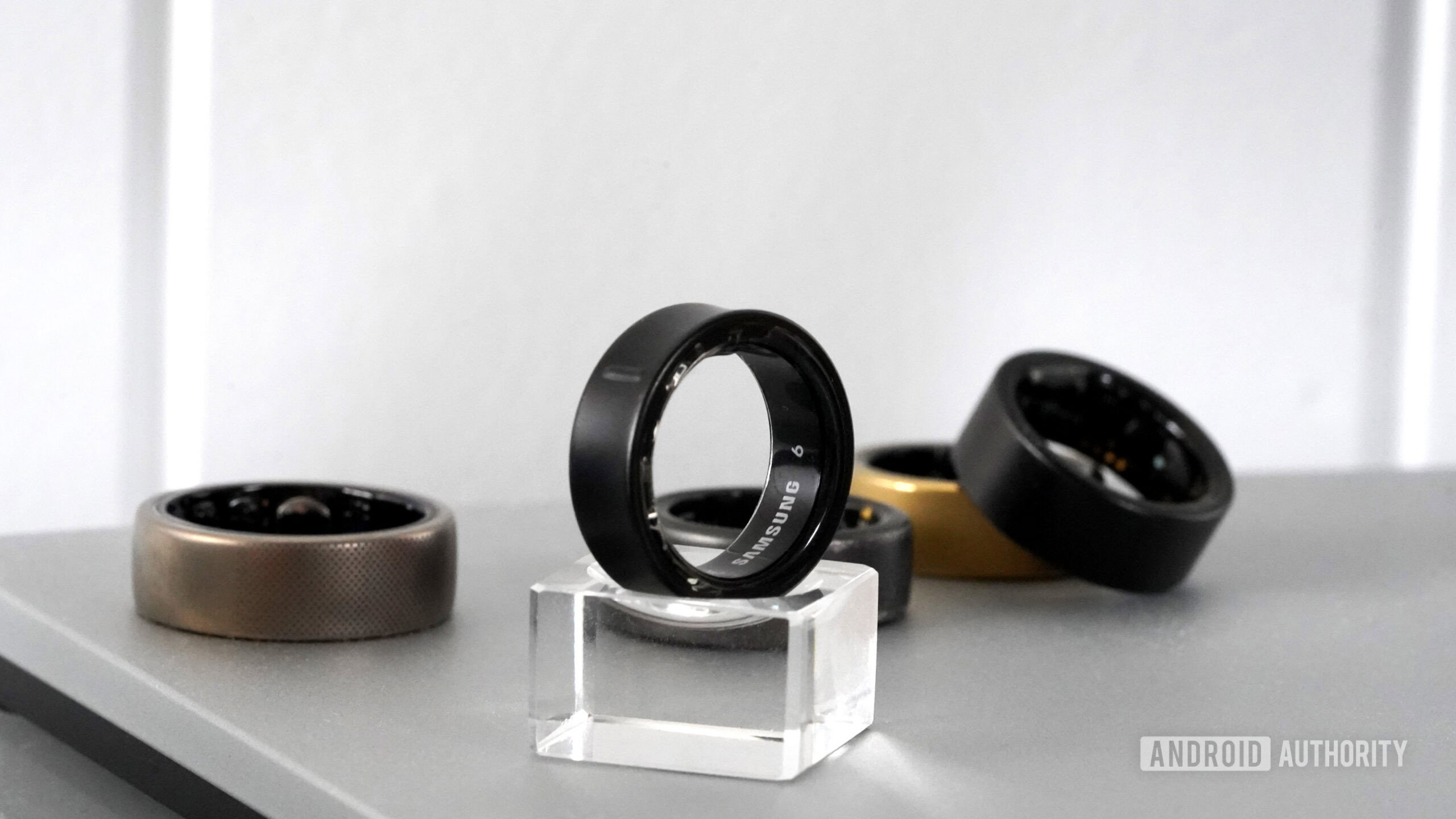 Samsung Galaxy Ring Design A Samsung Galaxy Ring rests on a small stand in front of alternative smart rings.
